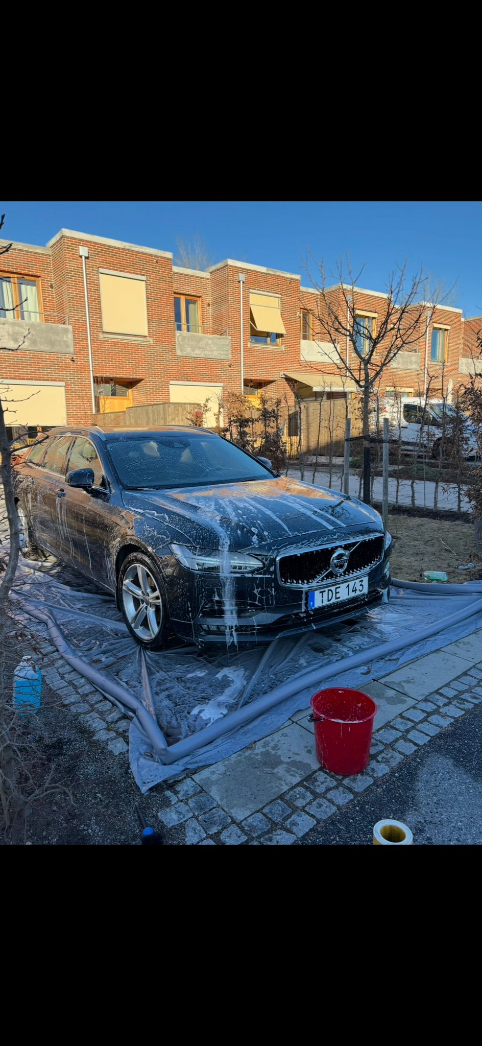 Mörkblå Volvo S90 täckt av skum under utvändig rekond i solsken
